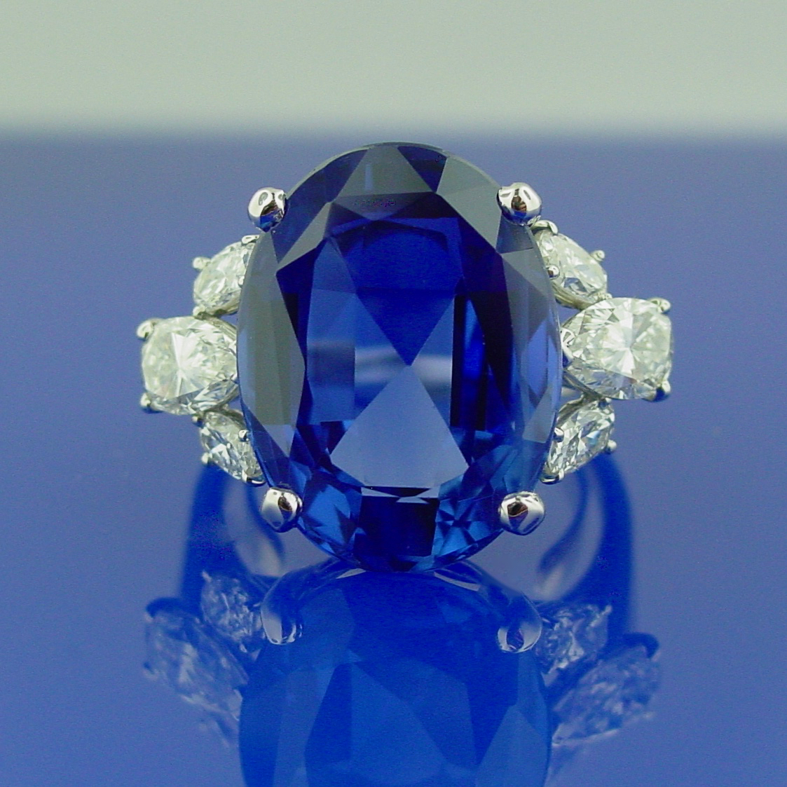 A blue sapphire and diamond ring is shown on top of a mirror.