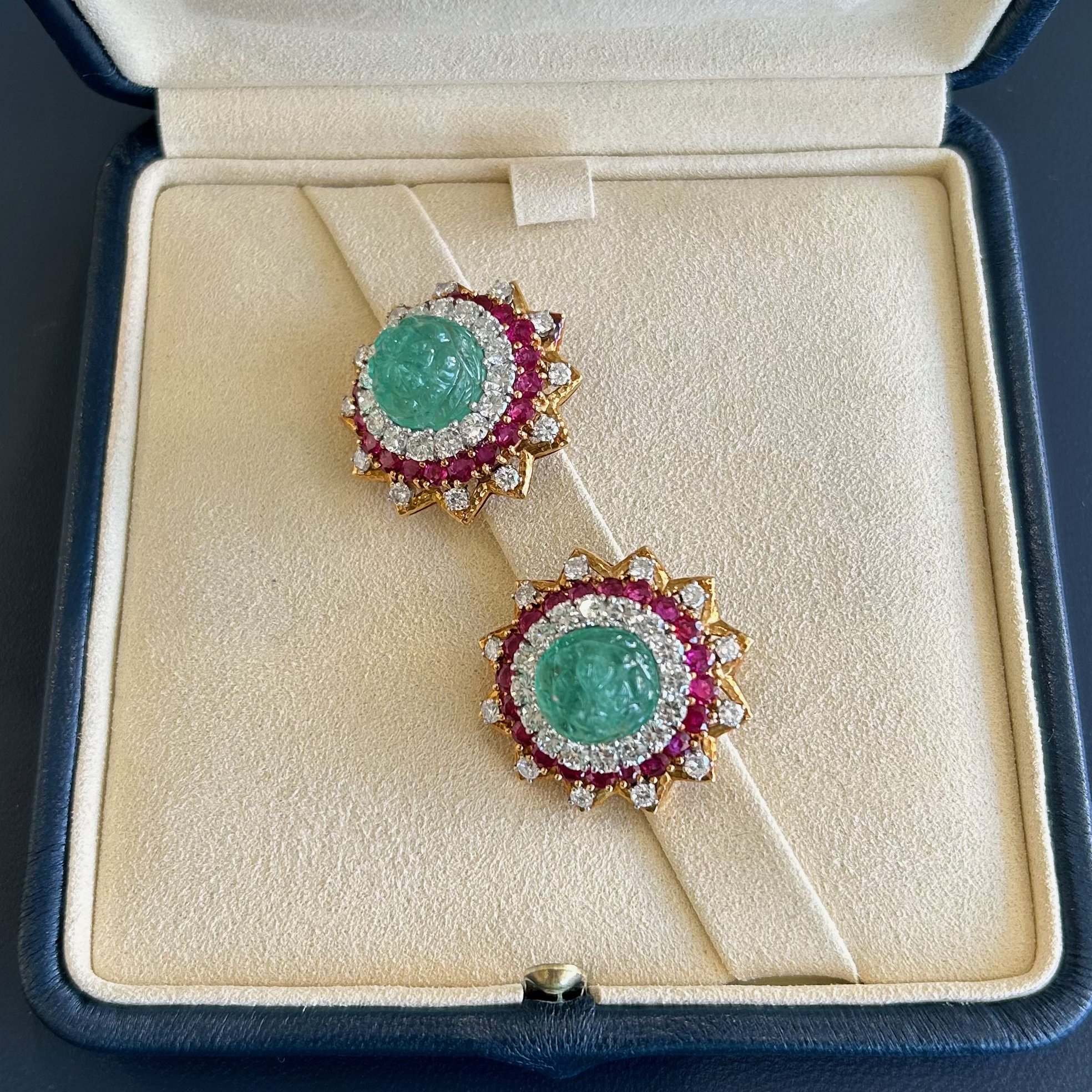 A pair of earrings in a box with a green stone.